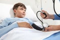 Child lying in bed in hospital room and nurse measuring his pressure with sphygmomanometer and stethoscope Royalty Free Stock Photo